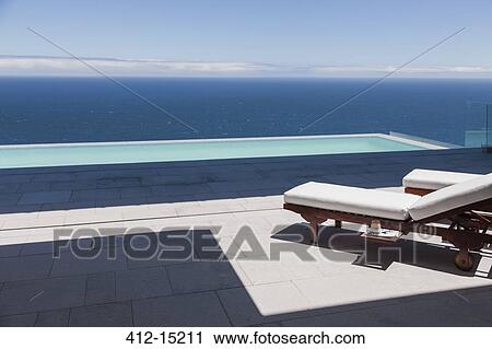 Stock Image - Lounge chairs and infinity pool overlooking ocean. Fotosearch