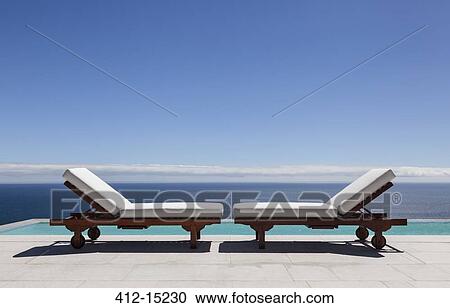 Stock Image - Lounge chairs and infinity pool overlooking ocean. Fotosearch