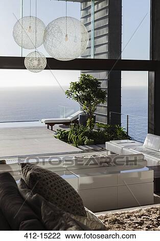 Stock Image - Sofas and tables in modern living room overlooking ocean. Fotosearch
