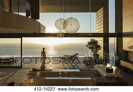 Stock Photo - Woman in modern house overlooking ocean. Fotosearch