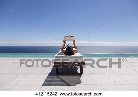 Woman reading on lounge chair at poolside overlooking ocean View Large Photo Image Stock Image - Woman reading on lounge chair at poolside overlooking ocean. Fotosearch