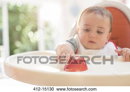 Stock Image - Baby boy eating in high chair. Fotosearch
