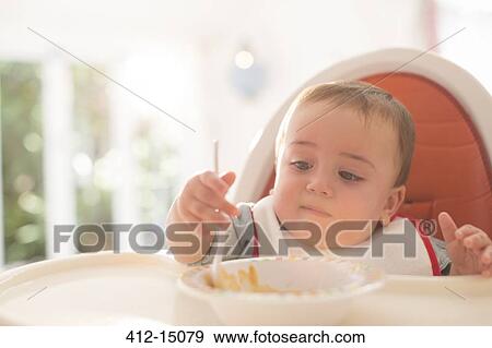 Baby boy eating in high chair View Large Photo Image Stock Photo - Baby boy eating in high chair. Fotosearch