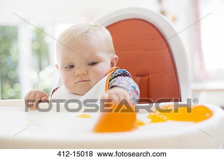 Stock Photo - Baby girl eating in high chair. Fotosearch