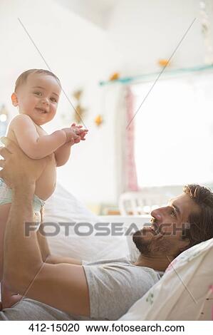 Stock Image - Father holding baby boy on sofa. Fotosearch