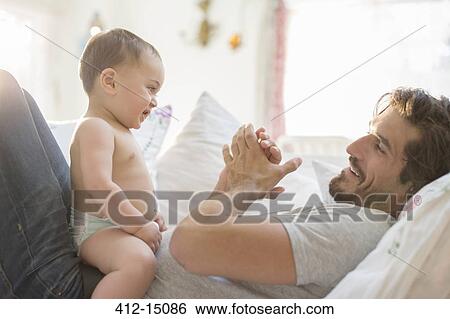 Stock Photograph - Father playing with baby son on sofa. Fotosearch
