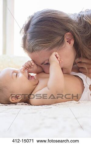 Stock Image - Mother blowing raspberries on baby's stomach. Fotosearch