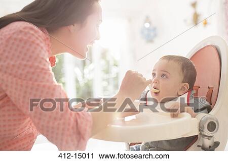 Mother feeding baby boy in high chair View Large Photo Image Stock Image - Mother feeding baby boy in high chair. Fotosearch