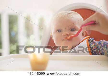 Mother feeding baby girl in high chair View Large Photo Image Stock Photo - Mother feeding baby girl in high chair. Fotosearch