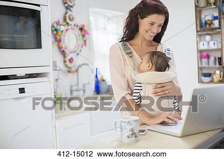 Mother holding baby boy and using laptop in domestic kitchen View Large Photo Image Stock Image - Mother holding baby boy and using laptop in domestic kitchen. Fotosearch