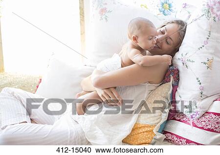 Stock Image - Mother holding baby boy on bed. Fotosearch