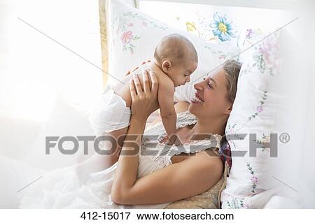 Mother holding baby boy on bed View Large Photo Image Stock Photo - Mother holding baby boy on bed. Fotosearch