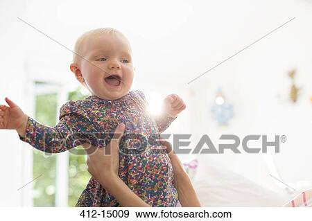 Stock Photo - Mother holding baby girl in living room. Fotosearch