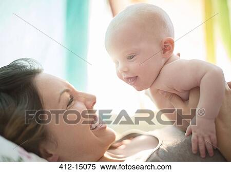 Stock Photography - Mother holding baby girl on bed. Fotosearch