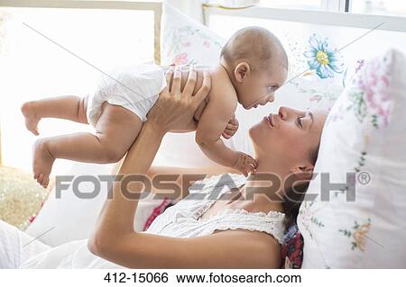 Stock Photograph - Mother playing with baby boy on bed. Fotosearch