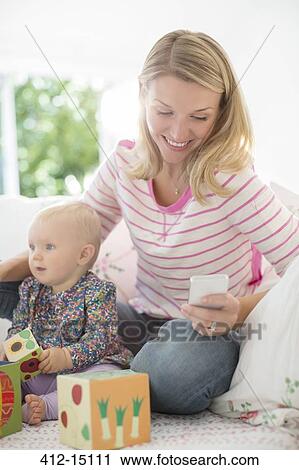 Mother playing with baby girl and checking cell phone View Large Photo Image Stock Image - Mother playing with baby girl and checking cell phone. Fotosearch