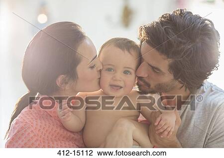 Stock Image - Parents kissing baby boy's cheeks. Fotosearch