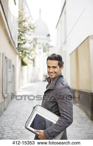 Stock Image - Businessman carrying digital tablet on city street. Fotosearch