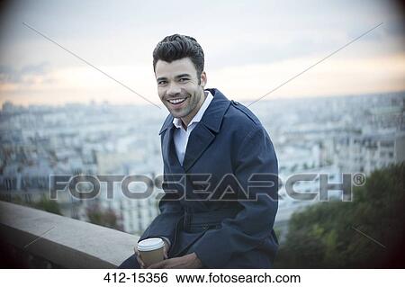 Stock Photograph - Businessman drinking coffee on ledge overlooking Paris, France. Fotosearch