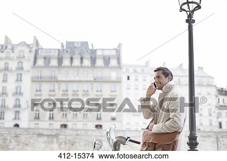 Businessman on bicycle talking on cell phone in Paris, France View Large Photo Image Picture - Businessman on bicycle talking on cell phone in Paris, France. Fotosearch
