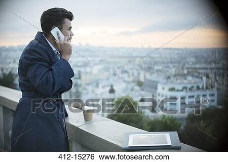 Stock Photograph - Businessman on cell phone overlooking Paris, France. Fotosearch