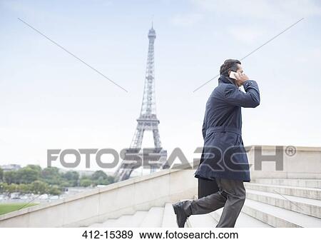 Stock Photo - Businessman talking on cell phone and ascending steps near Eiffel Tower, Paris, France. Fotosearch