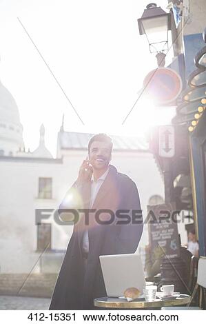 Stock Image - Businessman talking on cell phone at sidewalk cafe. Fotosearch
