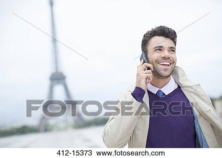 Stock Image - Businessman talking on cell phone by Eiffel Tower. Fotosearch