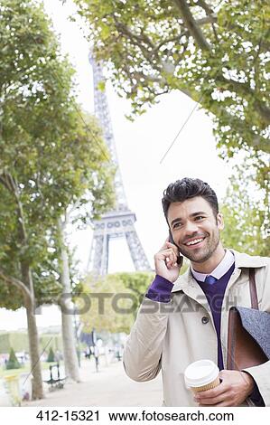 Stock Image - Businessman talking on cell phone near Eiffel Tower, Paris, France. Fotosearch