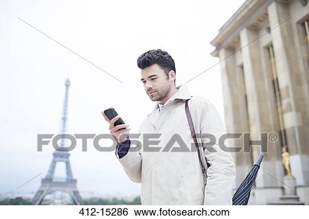 Stock Photograph - Businessman using cell phone by Eiffel Tower, Paris, France. Fotosearch