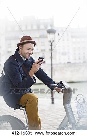 Stock Photography - Businessman using cell phone on bicycle along Seine River, Paris, France. Fotosearch