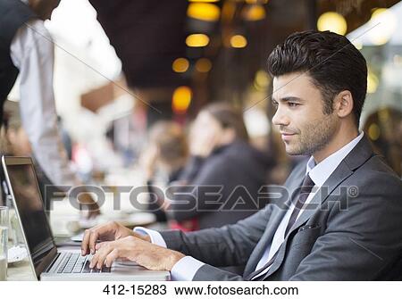 Stock Image - Businessman using laptop at sidewalk cafe. Fotosearch