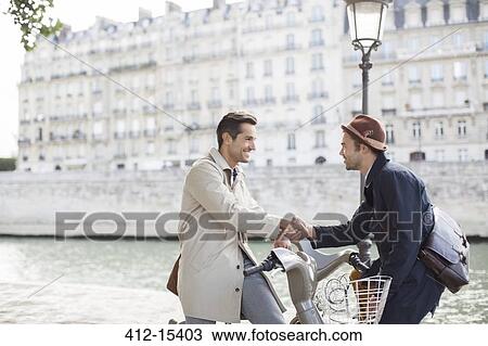 Stock Image - Businessmen handshaking on bicycles along Seine River, Paris, France. Fotosearch