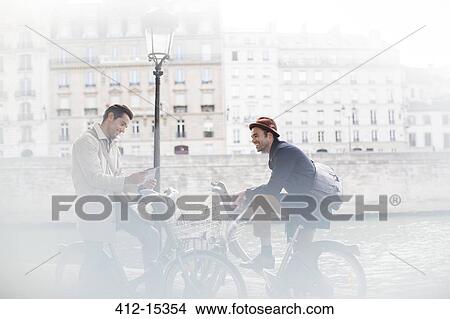 Businessmen talking on bicycles along Seine River, Paris, France View Large Photo Image Picture - Businessmen talking on bicycles along Seine River, Paris, France. Fotosearch