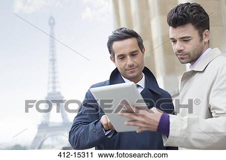 Stock Image - Businessmen using digital tablet near Eiffel Tower, Paris, France. Fotosearch
