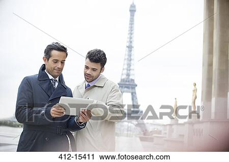 Stock Image - Businessmen using digital tablet near Eiffel Tower, Paris, France. Fotosearch
