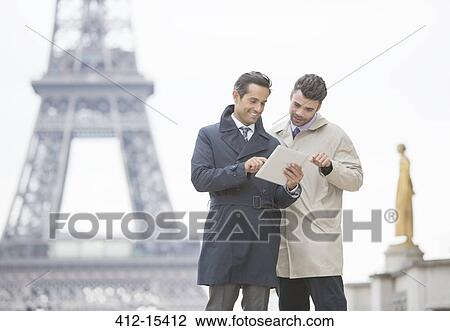 Stock Image - Businessmen using digital tablet near Eiffel Tower, Paris, France. Fotosearch