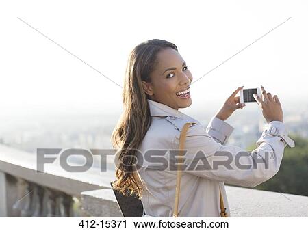Stock Image - Businesswoman taking pictures with cell phone outdoors. Fotosearch