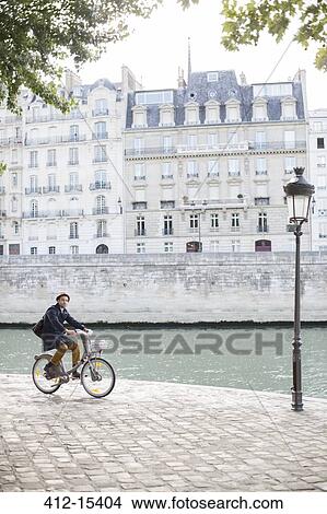 Picture - Man riding bicycle along Seine River, Paris, France. Fotosearch