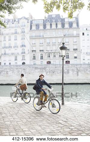 Stock Photograph - Men riding bicycles along Seine River, Paris, France. Fotosearch