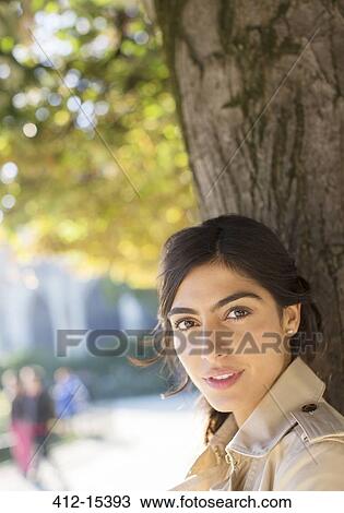 Woman standing against tree trunk in urban park View Large Photo Image Stock Image - Woman standing against tree trunk in urban park. Fotosearch