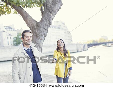 Picture - Couple holding hands along Seine River, Paris, France. Fotosearch
