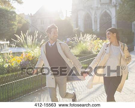 Stock Image - Couple holding hands and running in urban park. Fotosearch