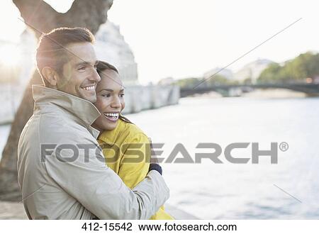 Stock Image - Couple hugging along Seine River, Paris, France. Fotosearch