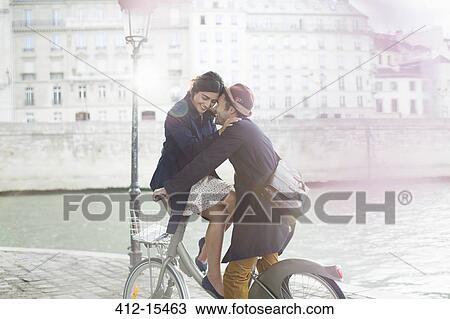 Stock Image - Couple hugging on bicycle along Seine River, Paris, France. Fotosearch