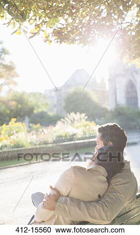 Stock Image - Couple hugging on park bench. Fotosearch