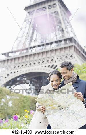 Stock Photo - Couple reading map in front of Eiffel Tower, Paris, France. Fotosearch