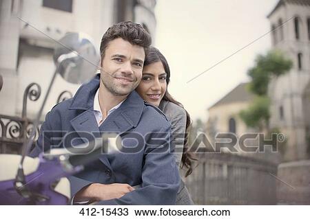 Couple sitting on scooter on city street View Large Photo Image Stock Image - Couple sitting on scooter on city street. Fotosearch