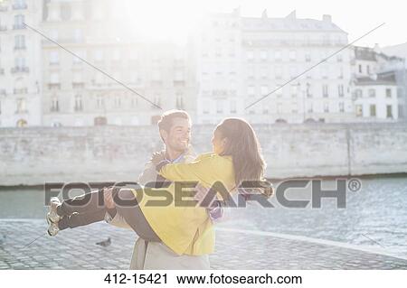 Stock Image - Man holding girlfriend along Seine River, Paris, France. Fotosearch