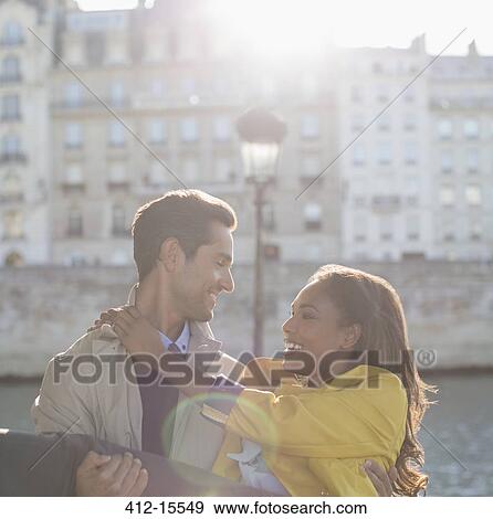 Stock Photo - Man holding girlfriend along Seine River, Paris, France. Fotosearch